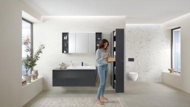 Une femme ouvre un meuble haut avec beaucoup d'espace de rangement dans une salle de bains équipée de meubles de salle de bains Geberit Acanto.